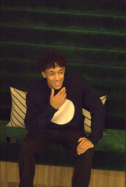 Laughing, seated on a green bench in the Merino Knit.